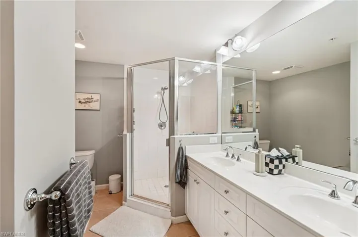 Bathroom with double vanity, a shower stall, light tile patterned floors, and recessed lighting