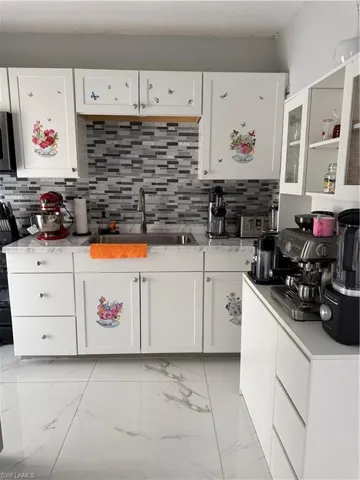 Kitchen featuring white cabinets, glass insert cabinets, light marble finish floors, and decorative backsplash