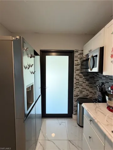 Kitchen with black microwave, white cabinetry, light marble finish floors, light stone counters, and decorative backsplash