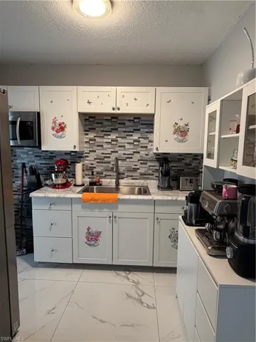 Kitchen featuring light marble finish flooring, backsplash, a textured ceiling, white cabinetry, and glass insert cabinets