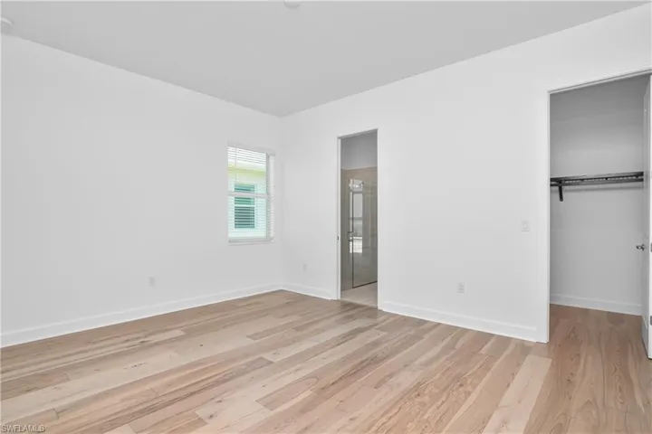 Unfurnished bedroom with a walk in closet, light wood-type flooring, and ensuite bath
