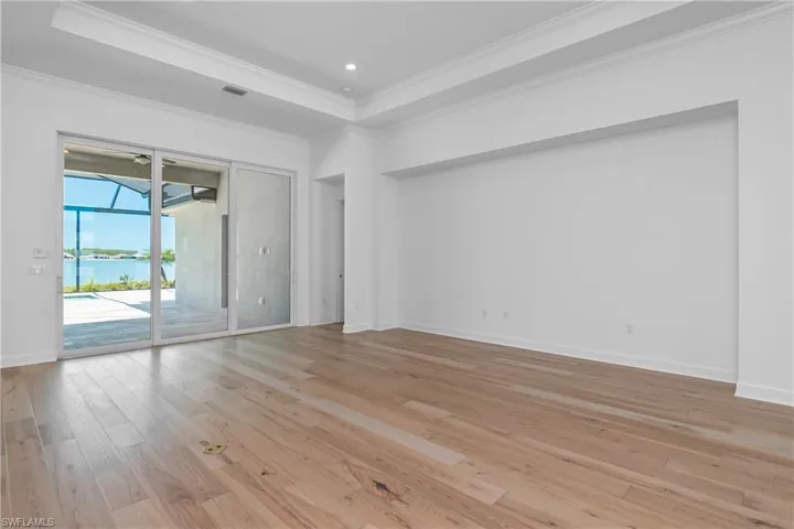 Spare room featuring a tray ceiling, light wood-style flooring, ornamental molding, and a water view