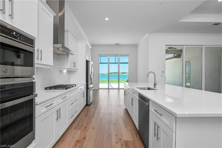 Kitchen with crown molding, stainless steel appliances, a kitchen island with sink, light wood-style floors, and white cabinets