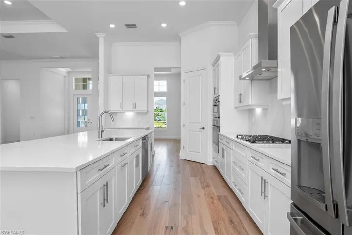 Kitchen featuring crown molding, stainless steel appliances, light wood-style flooring, white cabinets, and an island with sink