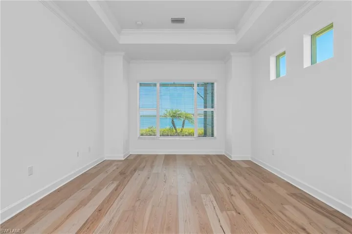 Unfurnished room featuring light wood-style flooring, a raised ceiling, and crown molding