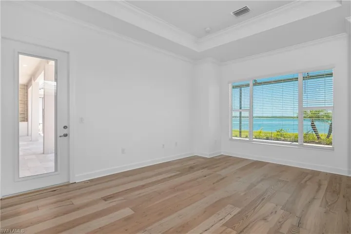 Spare room featuring a tray ceiling, light wood-style floors, and crown molding