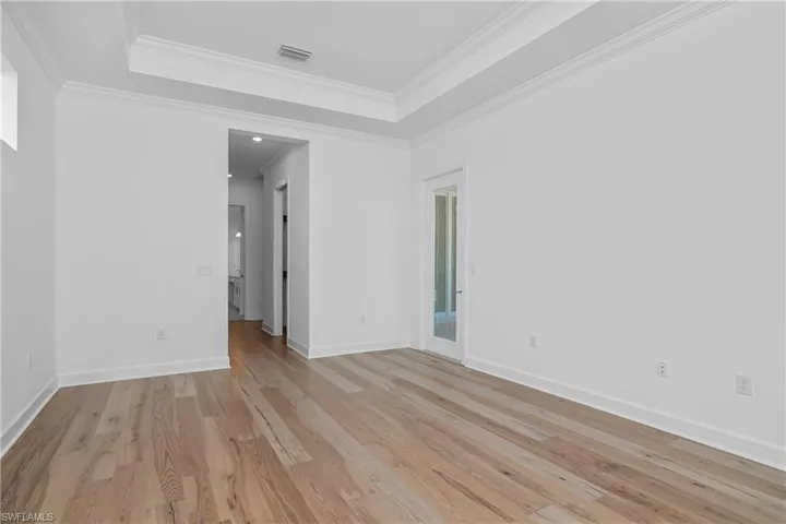 Unfurnished room with a tray ceiling, light wood-style floors, and ornamental molding