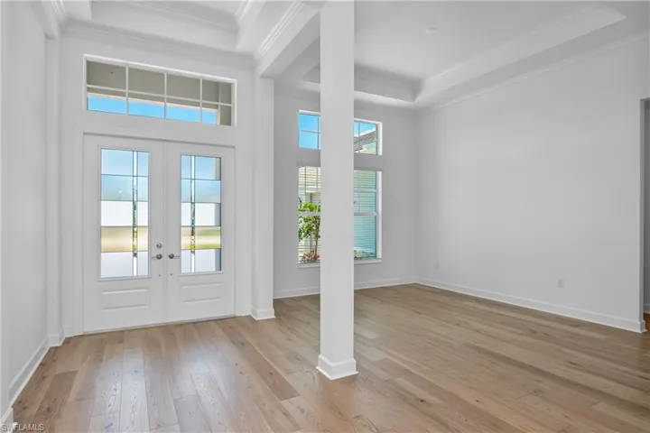 Foyer featuring crown molding, light wood finished floors, french doors, and a raised ceiling