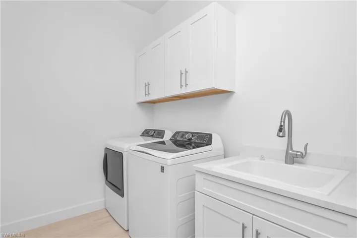 Laundry room with washer and clothes dryer, cabinet space, and light wood-style floors