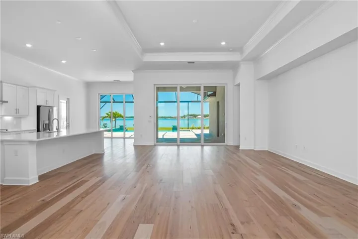 Unfurnished living room featuring light wood-type flooring, a tray ceiling, crown molding, a water view, and recessed lighting