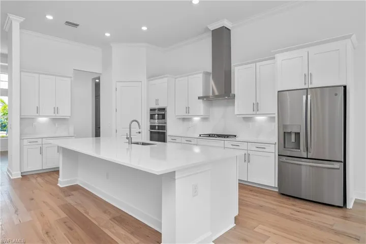 Kitchen with stainless steel appliances, crown molding, white cabinets, light wood-style flooring, and recessed lighting