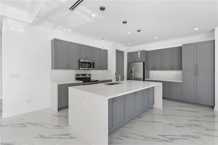 Kitchen with gray cabinetry, stainless steel appliances, hanging light fixtures, light stone countertops, and recessed lighting