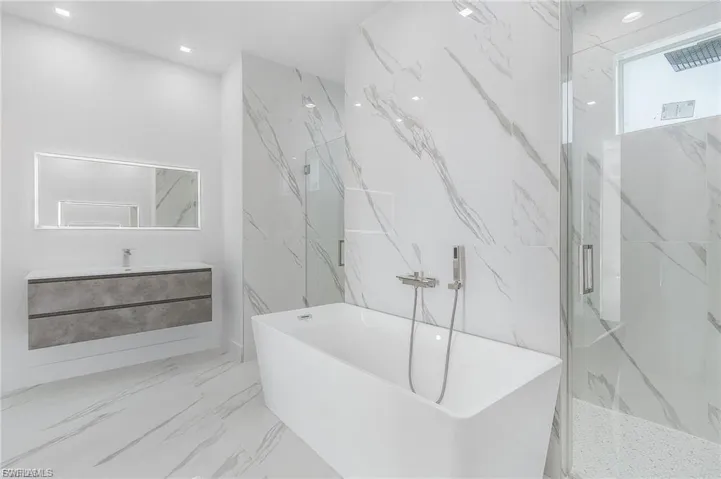 Bathroom with a freestanding tub, vanity, marble tiled floors, a marble finish shower, and stone wall