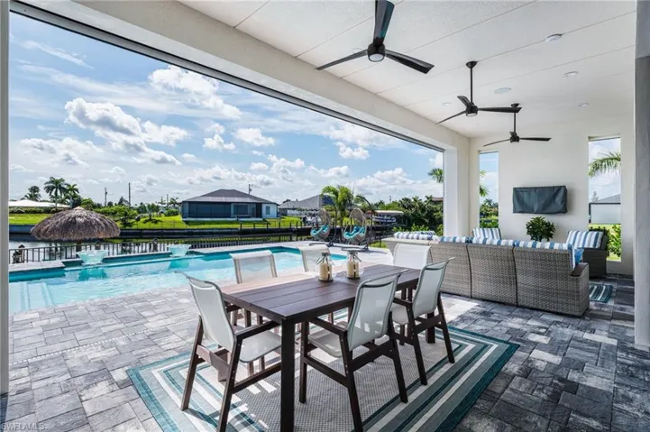 Expansive covered patio featuring a paver deck, multiple ceiling fans, and an integrated swimming pool with a waterfront setting