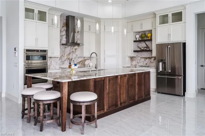 Spacious kitchen featuring an expansive center island with seating, stainless steel appliances, white upper cabinetry, and a granite backsplash