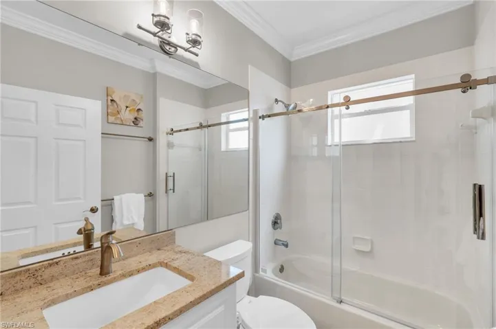 Full bathroom featuring vanity, crown molding, bath / shower combo with glass door, and toilet