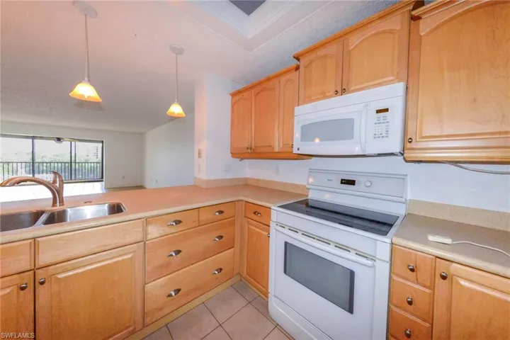 Kitchen with hanging light fixtures, sink, light tile patterned floors, and white appliances