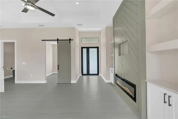 Unfurnished living room with a barn door, a fireplace, a ceiling fan, a raised ceiling, and recessed lighting