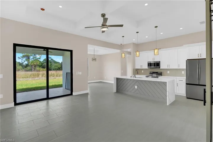Kitchen with white cabinets, coffered ceiling, stainless steel appliances, light stone counters, and a center island with sink