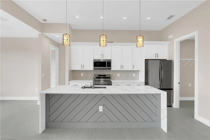 Kitchen with light stone countertops, stainless steel appliances, an island with sink, white cabinets, and backsplash