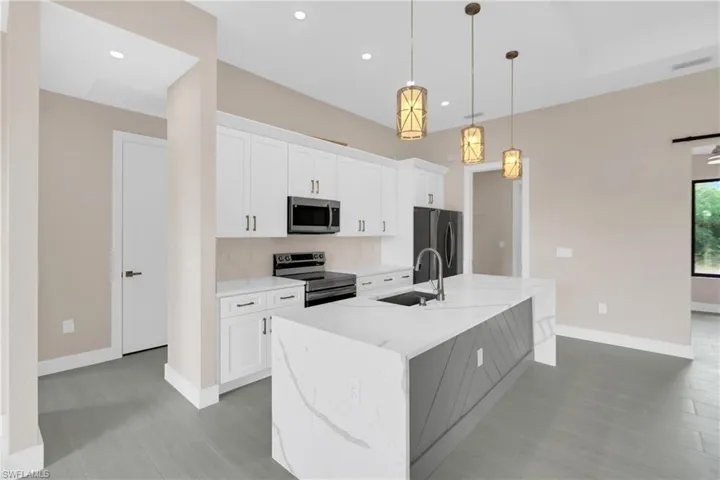 Kitchen featuring white cabinets, stainless steel appliances, light stone counters, a center island with sink, and pendant lighting