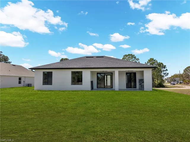 Back of house featuring a lawn and stucco siding