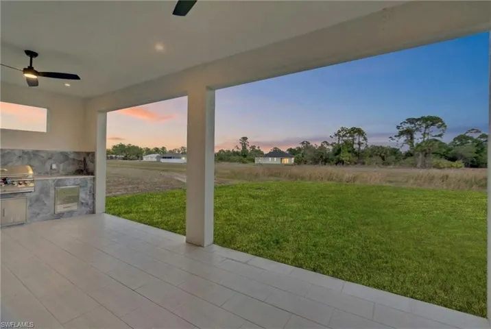 Patio terrace at dusk with an outdoor kitchen, a lawn, ceiling fan, and a patio