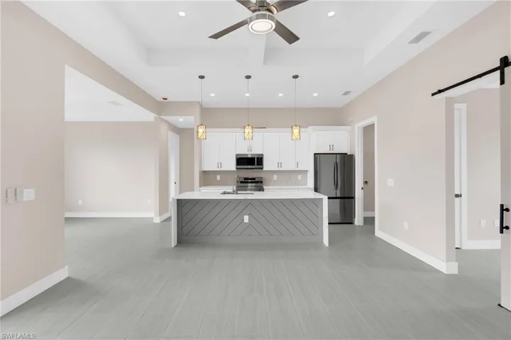Kitchen featuring a barn door, white cabinets, stainless steel appliances, light stone counters, and ceiling fan
