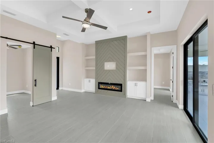 Unfurnished living room featuring a barn door, ceiling fan, built in shelves, coffered ceiling, and a large fireplace