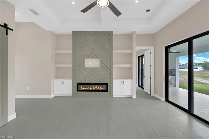 Unfurnished living room featuring ceiling fan, a barn door, a fireplace, built in features, and a tray ceiling