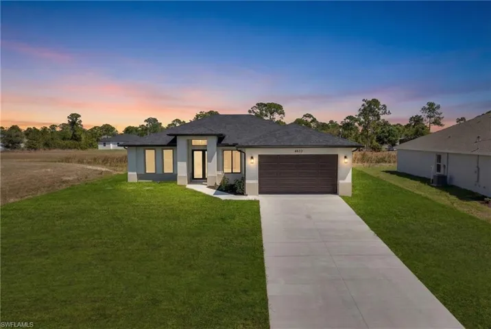 View of front of property with a front yard, concrete driveway, an attached garage, and stucco siding