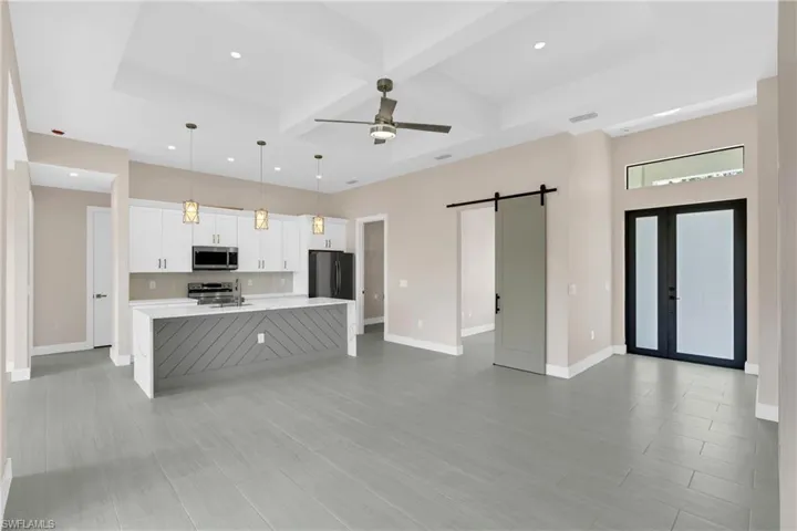 Kitchen featuring a barn door, white cabinetry, coffered ceiling, a spacious island, and hanging light fixtures