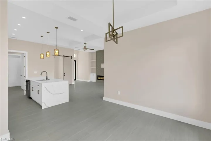 Kitchen featuring a fireplace, open floor plan, a barn door, hanging light fixtures, and a center island with sink
