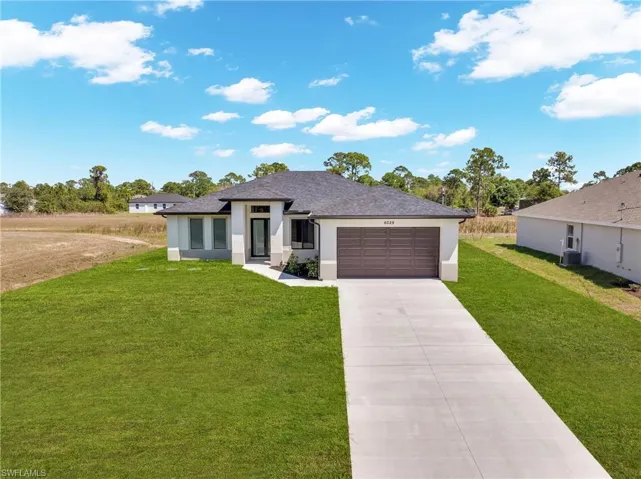 Prairie-style home featuring stucco siding, a front yard, concrete driveway, a garage, and roof with shingles