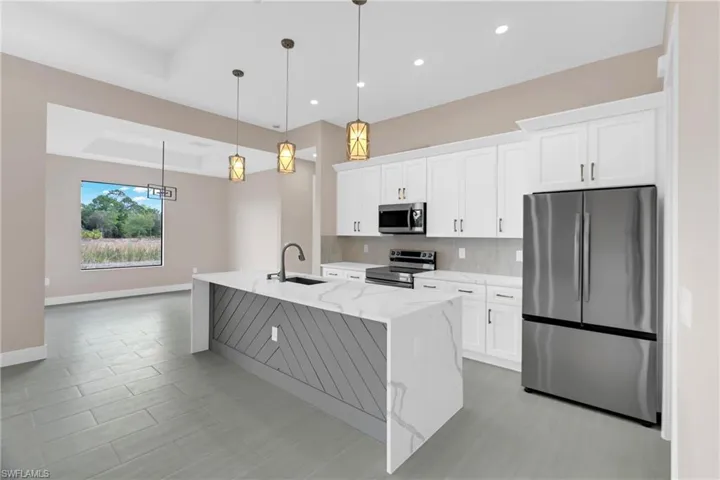 Kitchen with stainless steel appliances, white cabinetry, light stone counters, a kitchen island with sink, and hanging light fixtures
