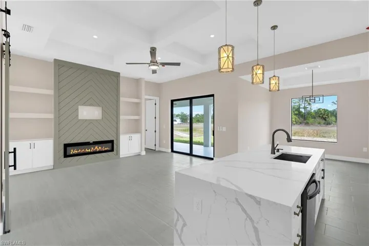 Kitchen featuring pendant lighting, plenty of natural light, coffered ceiling, light stone counters, and a fireplace