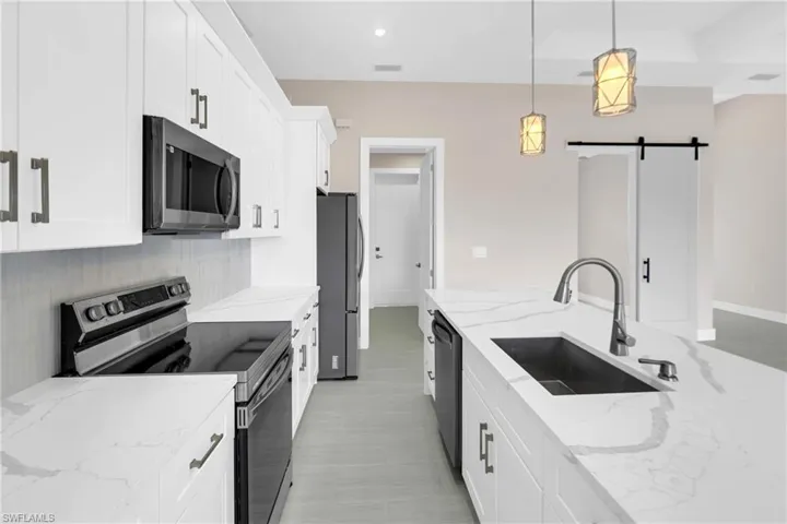 Kitchen with stainless steel appliances, light stone counters, white cabinetry, pendant lighting, and a barn door
