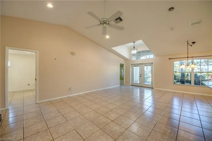 Tiled spare room with french doors, high vaulted ceiling, and ceiling fan with notable chandelier