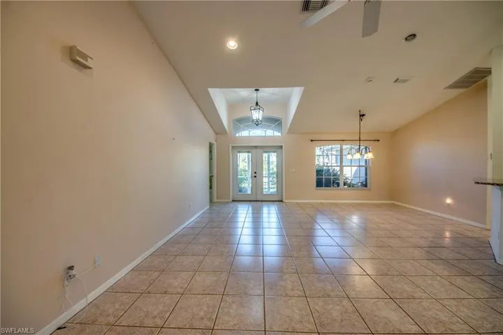 Tiled spare room with french doors, lofted ceiling, and ceiling fan with notable chandelier