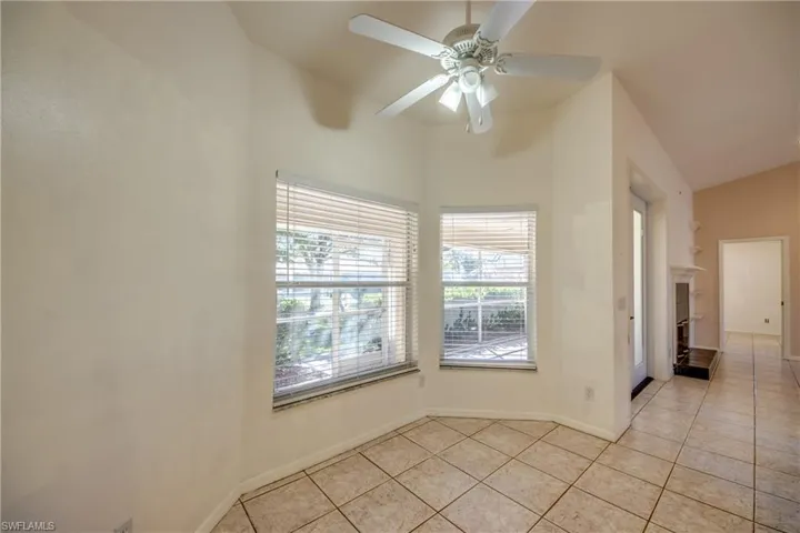 Spare room featuring a tiled fireplace, light tile patterned flooring, vaulted ceiling, and ceiling fan