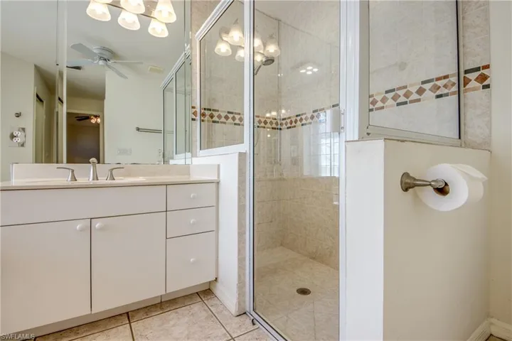 Bathroom featuring ceiling fan, tile patterned floors, vanity, and a tile shower