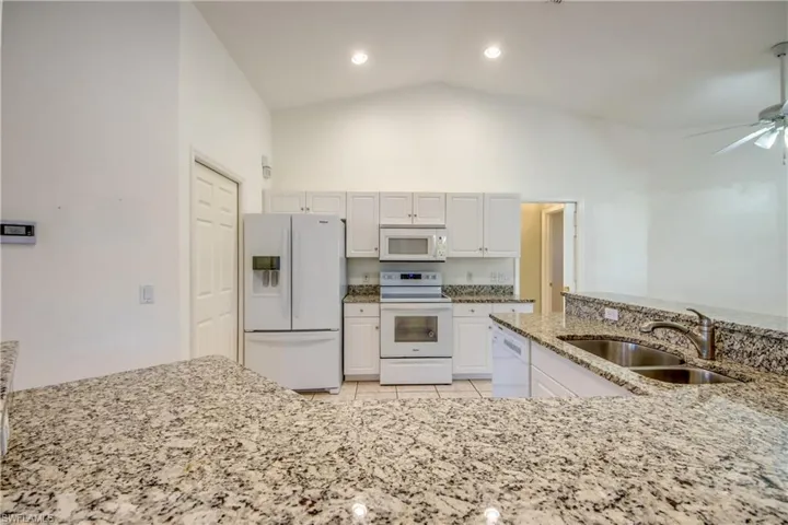 Kitchen with sink, white appliances, light stone countertops, and white cabinets