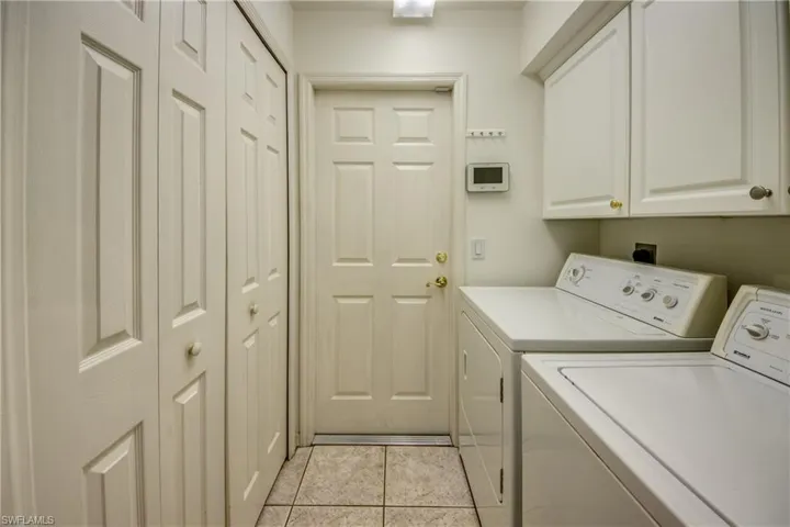 Laundry room with cabinets, light tile patterned floors, and washing machine and clothes dryer
