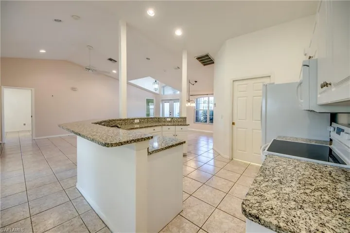 Kitchen with light tile patterned floors, white appliances, white cabinetry, a kitchen island, and vaulted ceiling