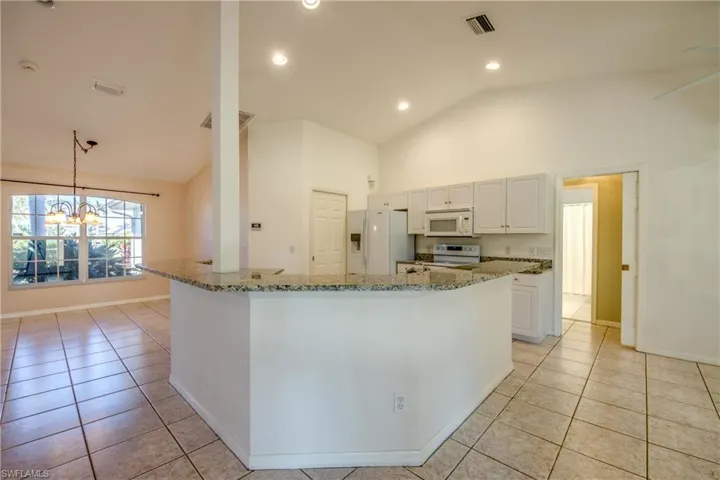Kitchen featuring light tile patterned floors, white cabinets, white appliances, and decorative light fixtures