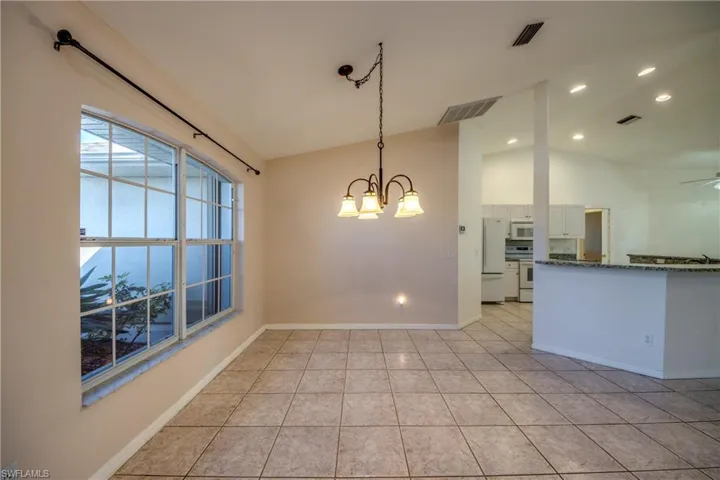 Unfurnished dining area with ceiling fan with notable chandelier, vaulted ceiling, and light tile patterned flooring