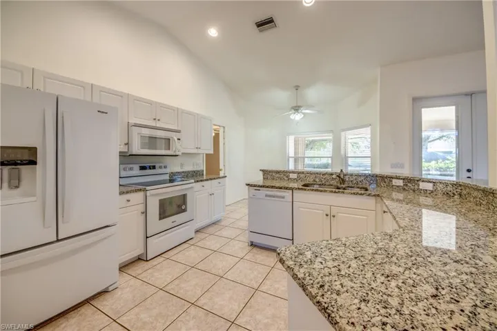 Kitchen featuring sink, white appliances, light tile patterned floors, white cabinetry, and light stone counters
