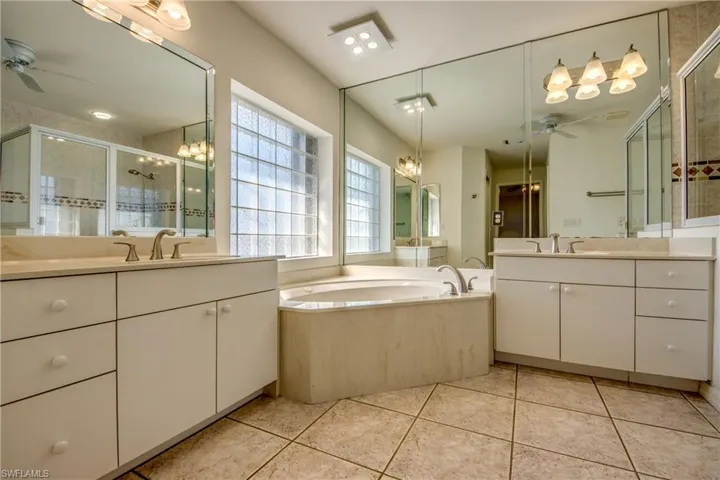 Bathroom featuring tile patterned flooring, vanity, ceiling fan with notable chandelier, and shower with separate bathtub