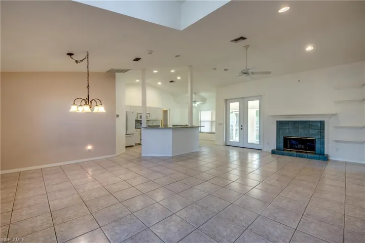 Unfurnished living room featuring light tile patterned flooring, ceiling fan with notable chandelier, high vaulted ceiling, a fireplace, and french doors
