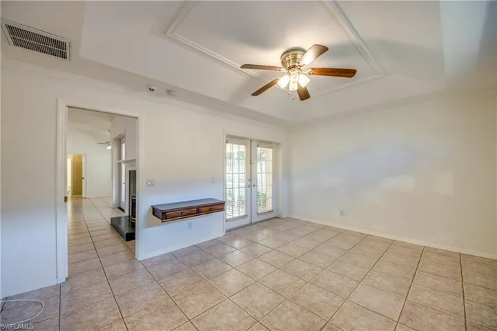Tiled empty room with a tray ceiling, ornamental molding, french doors, and ceiling fan